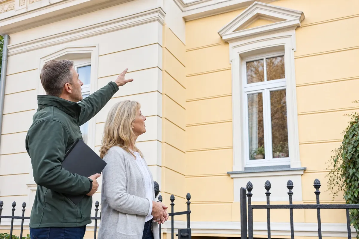 Ein Energieberater und eine Eigentümerin stehen vor einem für Bonn typischen Wohnhaus und sehen zum Dachrand hinauf.
