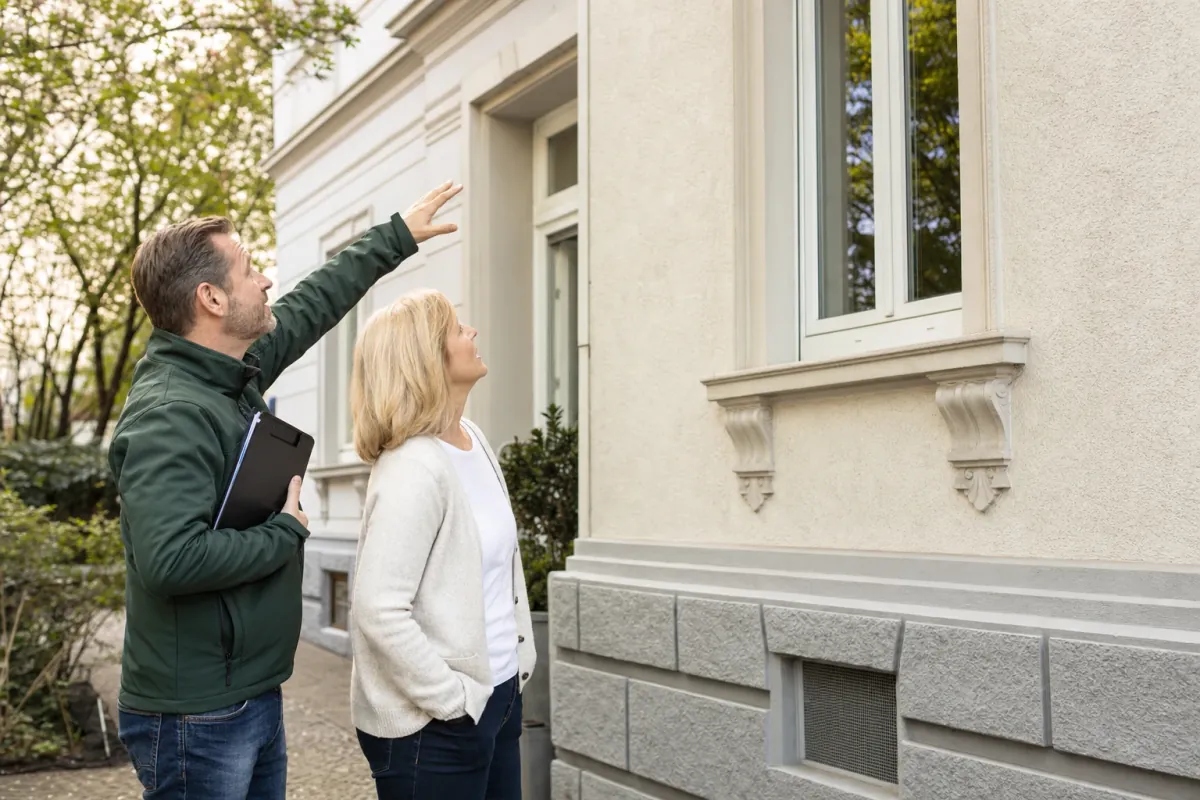 Ein Energieberater und eine Eigentümerin stehen vor einem für Wiesbaden typischen Wohnhaus und sehen zum Dachrand hinauf.
