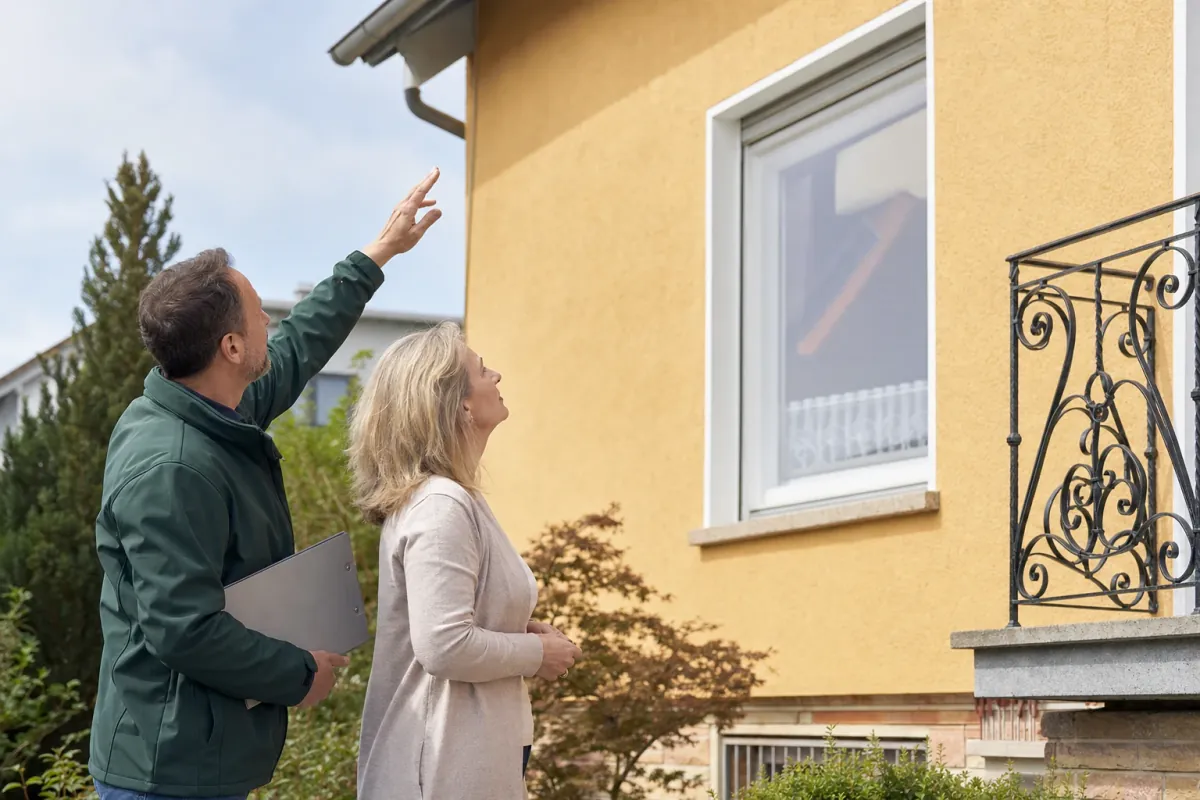 Ein Energieberater und eine Eigentümerin stehen vor einem für Würzburg typischen Wohnhaus und sehen zum Dachrand hinauf.
